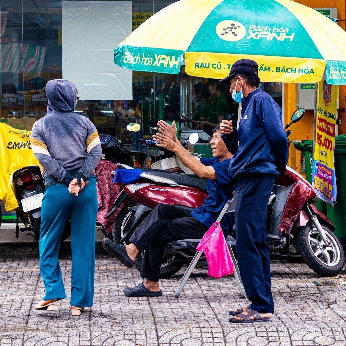 Three people standing and sitting near a scooter.